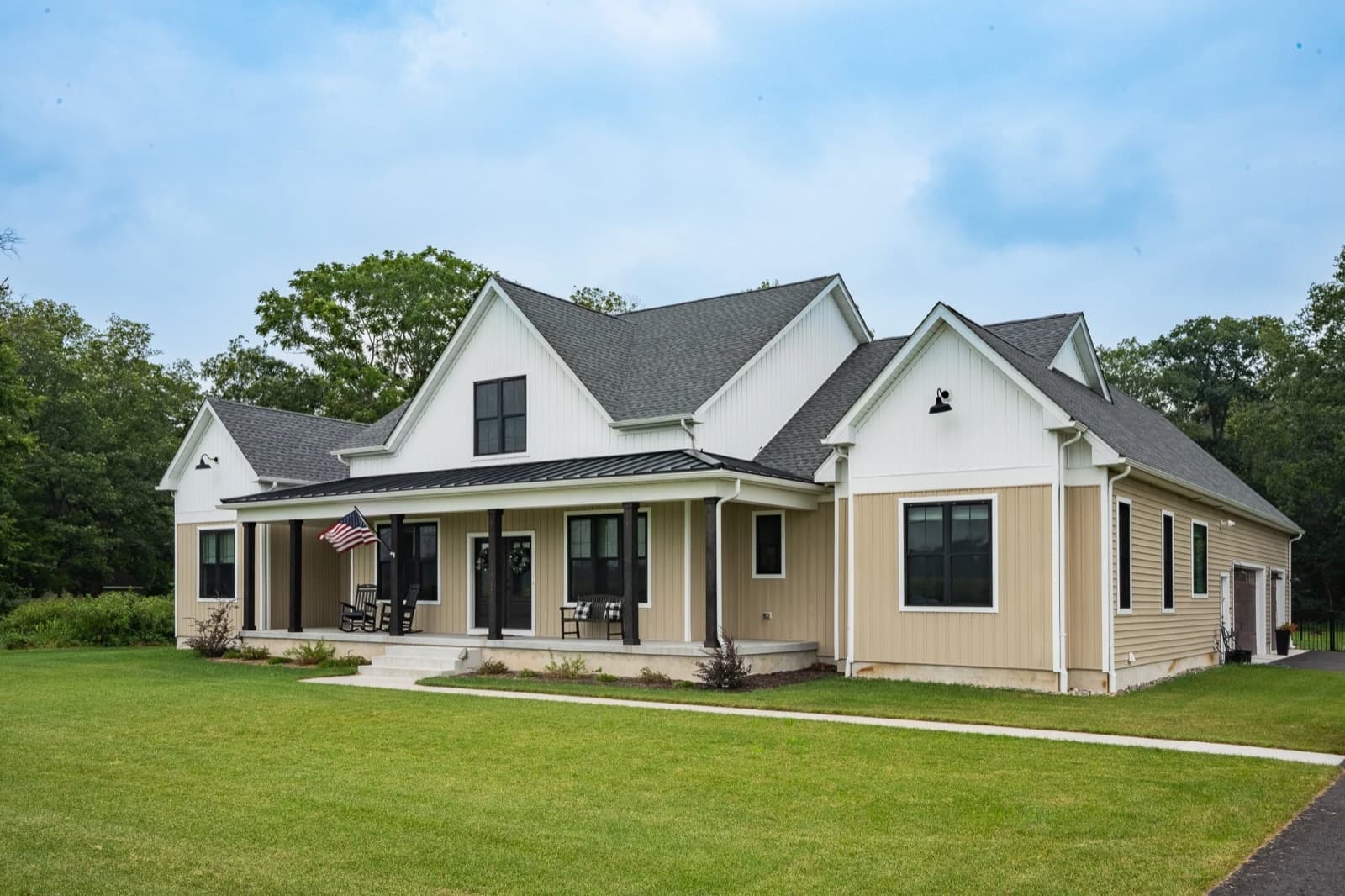 A white farmhouse with a deep covered porch and standing seam metal roof on an open lot