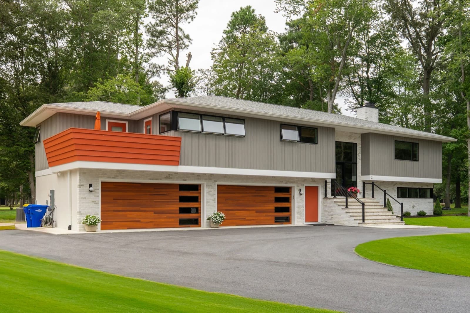A mid century split level house after renovation, with new cedar toned garage doors and a bright orange clad bay