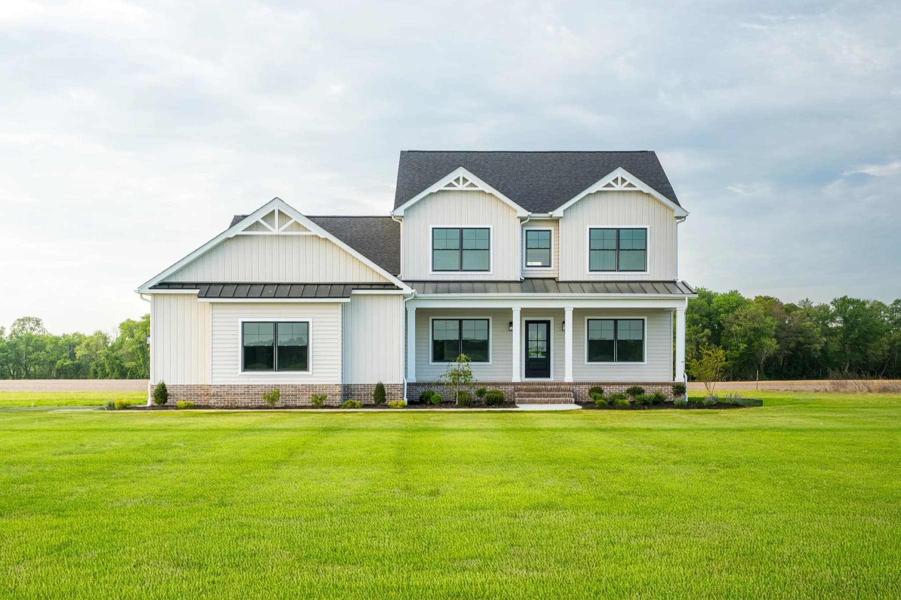 A low modern farmhouse in white board and batten with black framed windows and a wide mown lawn