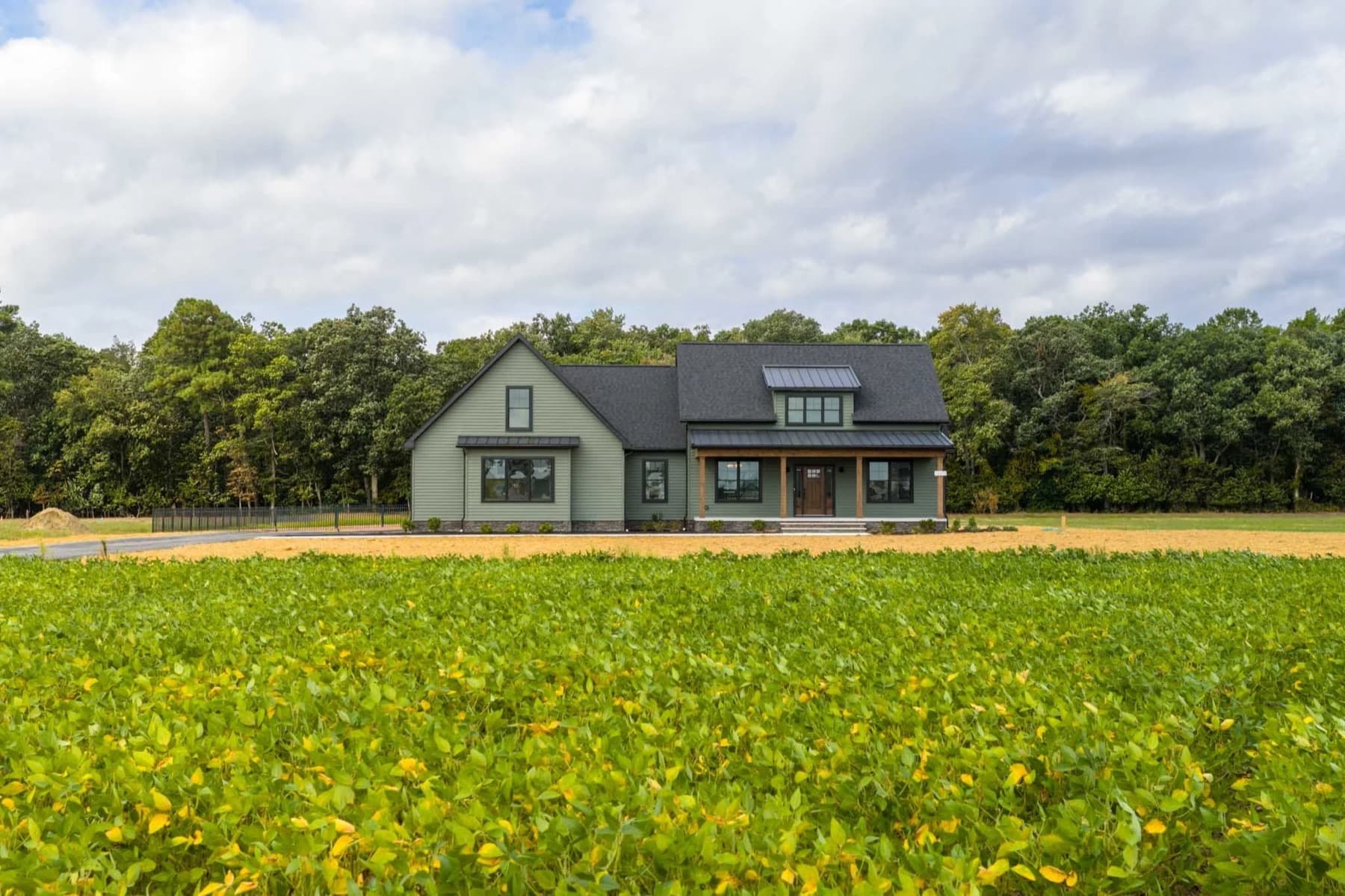 A sage green farmhouse seen across a soybean field under a broken sky