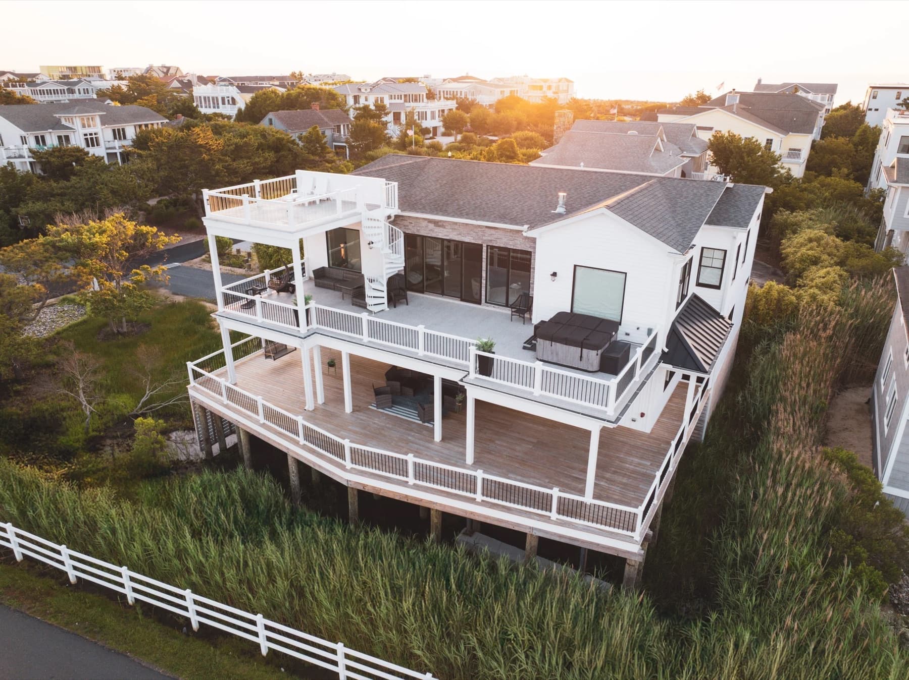 A coastal house with stacked decks and a pergola, photographed from the air at sunset